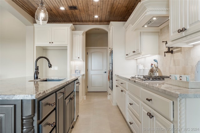 kitchen with custom exhaust hood, sink, light stone countertops, a center island with sink, and white cabinets