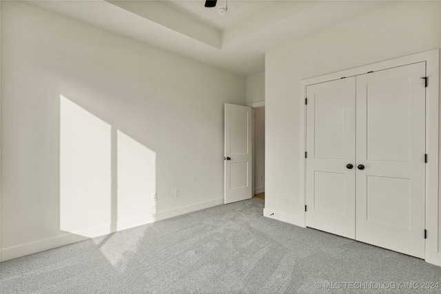 unfurnished bedroom with a closet, ceiling fan, a tray ceiling, and light carpet