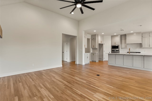 unfurnished living room featuring light wood-type flooring, high vaulted ceiling, and ceiling fan