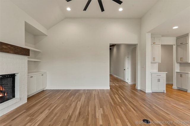 unfurnished living room with lofted ceiling, a brick fireplace, ceiling fan, and light hardwood / wood-style floors