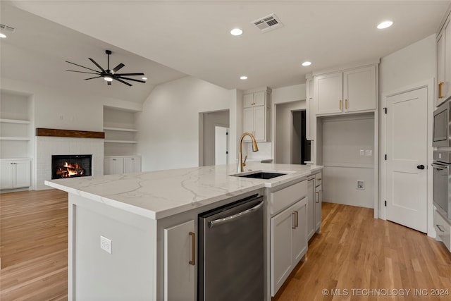 kitchen featuring a kitchen island with sink, light wood-type flooring, stainless steel appliances, light stone countertops, and ceiling fan