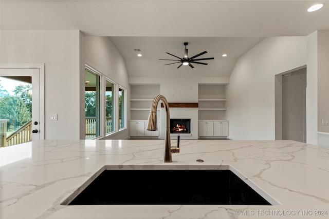 kitchen with built in features, sink, ceiling fan, light stone countertops, and lofted ceiling