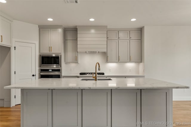 kitchen with light stone countertops, decorative backsplash, an island with sink, and light hardwood / wood-style flooring