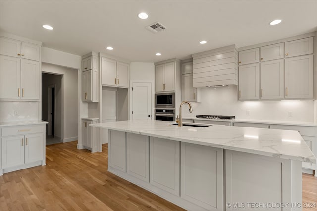 kitchen featuring light hardwood / wood-style flooring, backsplash, an island with sink, stainless steel appliances, and sink