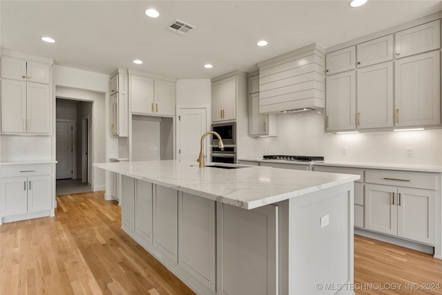 kitchen with backsplash, light hardwood / wood-style flooring, light stone counters, sink, and a kitchen island with sink