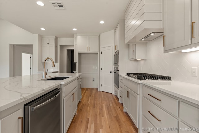 kitchen featuring light hardwood / wood-style flooring, appliances with stainless steel finishes, custom exhaust hood, white cabinetry, and sink