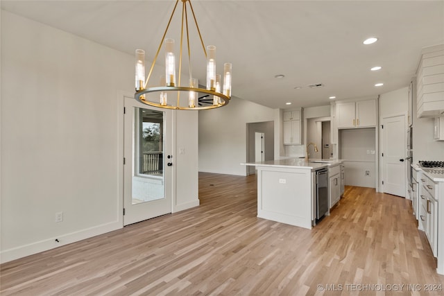 kitchen featuring pendant lighting, an island with sink, sink, white cabinetry, and light wood-type flooring