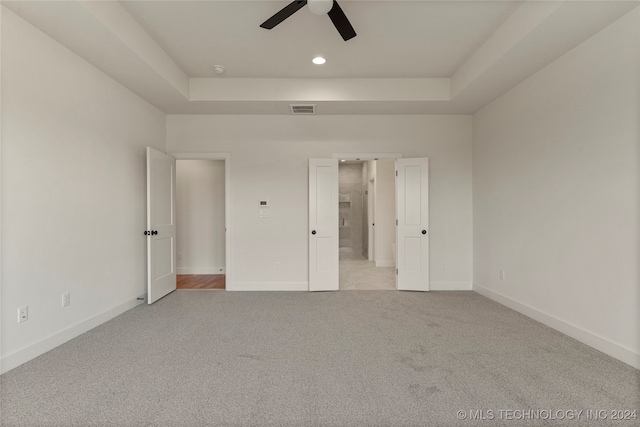 unfurnished bedroom featuring ceiling fan, light carpet, a tray ceiling, and connected bathroom