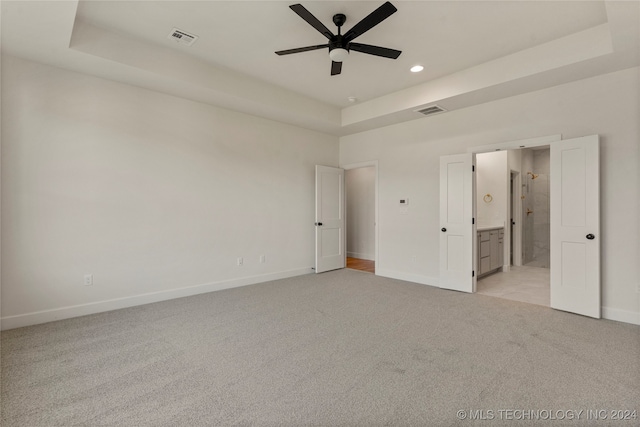 unfurnished bedroom featuring a tray ceiling, ceiling fan, light carpet, and ensuite bath