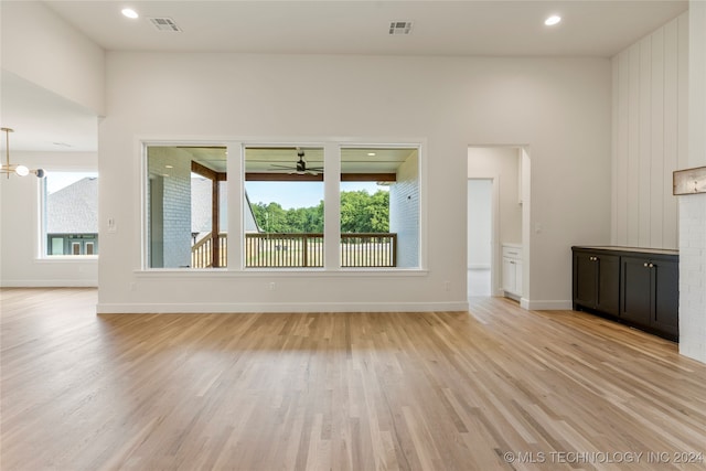 unfurnished living room featuring a healthy amount of sunlight, ceiling fan with notable chandelier, and light hardwood / wood-style floors