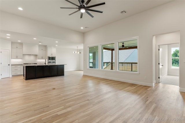 unfurnished living room featuring ceiling fan with notable chandelier and light hardwood / wood-style flooring