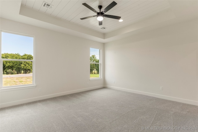 carpeted empty room featuring a tray ceiling, ceiling fan, a wealth of natural light, and wood ceiling