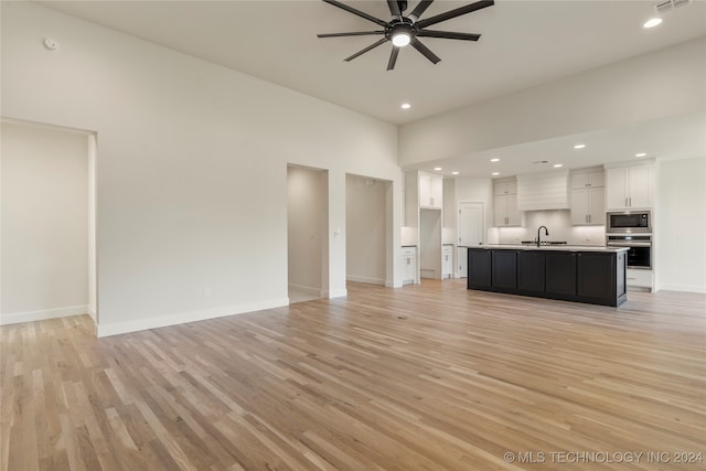 unfurnished living room featuring light hardwood / wood-style flooring, ceiling fan, and sink