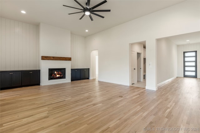 unfurnished living room featuring light hardwood / wood-style flooring, a high ceiling, and ceiling fan