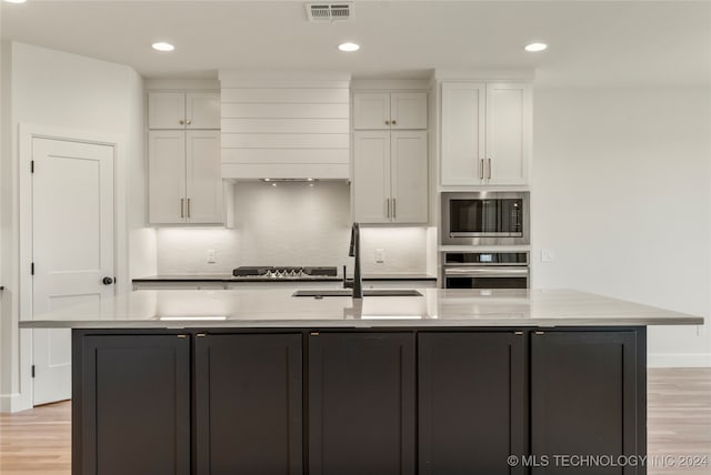 kitchen featuring white cabinets, stainless steel appliances, an island with sink, and sink