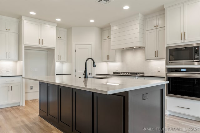 kitchen with light hardwood / wood-style floors, stainless steel appliances, and a center island with sink