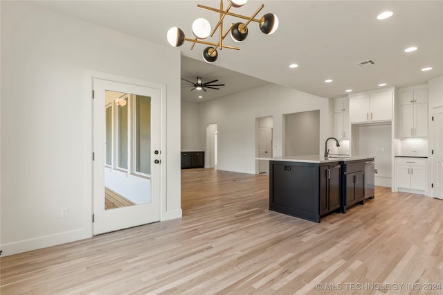 kitchen featuring white cabinets, ceiling fan with notable chandelier, light hardwood / wood-style floors, an island with sink, and pendant lighting