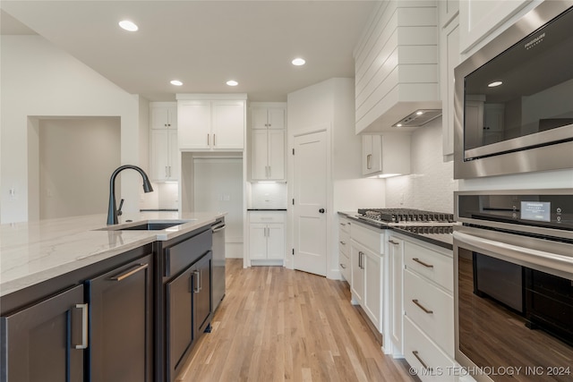 kitchen featuring custom range hood, stainless steel appliances, sink, light wood-type flooring, and white cabinets