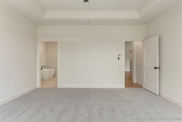 unfurnished bedroom featuring light colored carpet, a raised ceiling, ensuite bathroom, and wooden ceiling