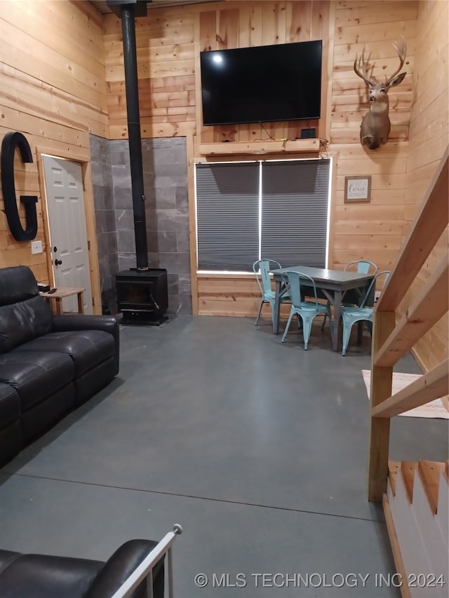 living room with concrete floors, a wood stove, and wooden walls