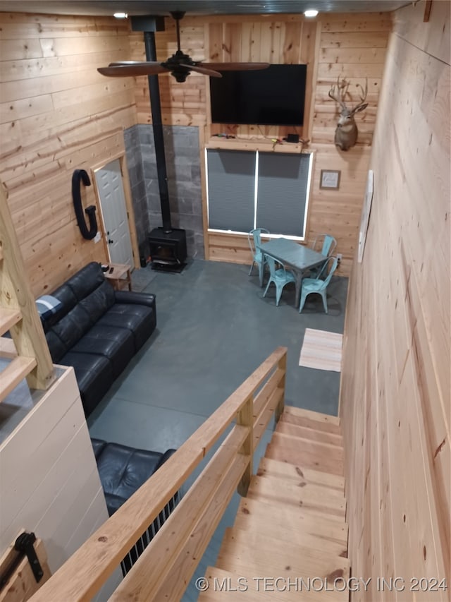 living room with wood walls, ceiling fan, and a wood stove