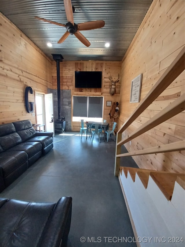 unfurnished living room featuring a wood stove, wood walls, and ceiling fan