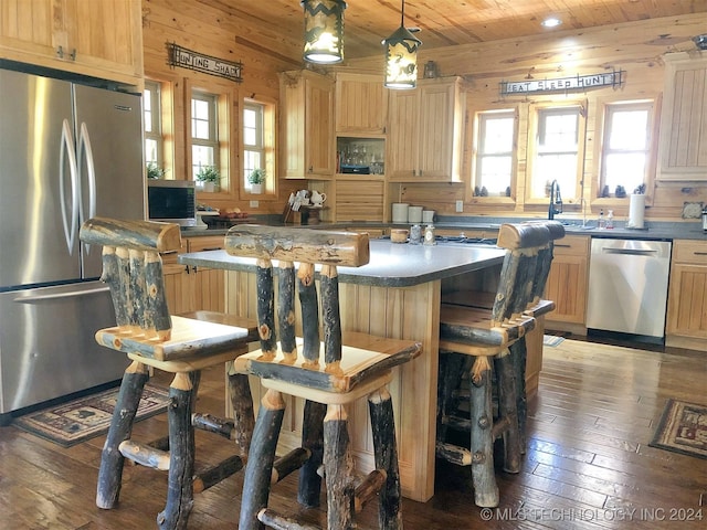 kitchen with decorative light fixtures, wood walls, light brown cabinetry, and stainless steel appliances