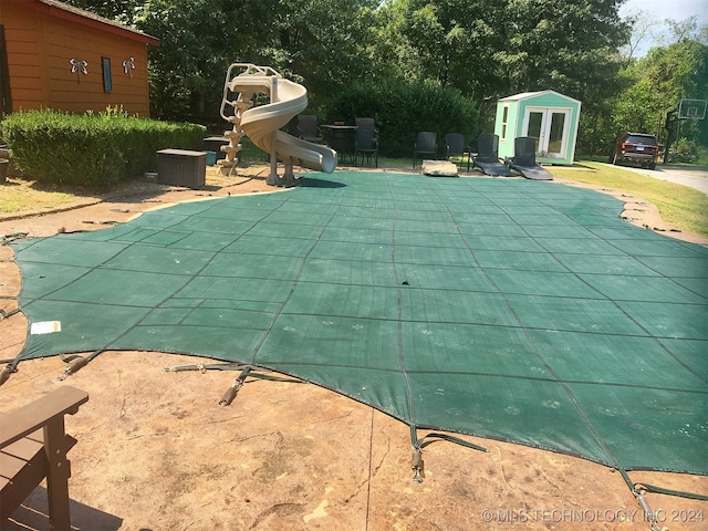 view of swimming pool with a water slide, an outbuilding, and a patio