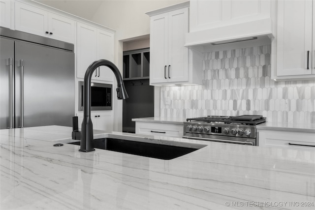 kitchen with white cabinets, custom range hood, light stone countertops, and high quality appliances