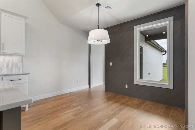 unfurnished dining area featuring light hardwood / wood-style flooring and wood walls