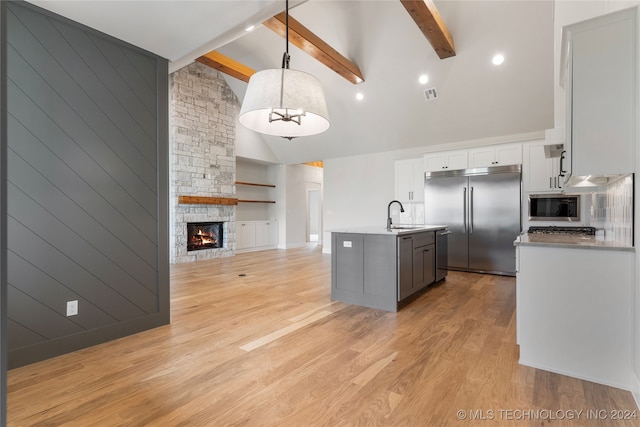 kitchen with light hardwood / wood-style flooring, beamed ceiling, a stone fireplace, built in appliances, and pendant lighting