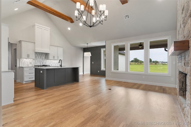 kitchen with light hardwood / wood-style floors, beamed ceiling, a notable chandelier, pendant lighting, and a kitchen island with sink