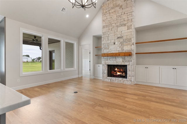 unfurnished living room with ceiling fan with notable chandelier, high vaulted ceiling, a fireplace, and light hardwood / wood-style floors