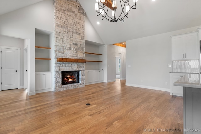 unfurnished living room with high vaulted ceiling, light hardwood / wood-style flooring, a notable chandelier, and a stone fireplace