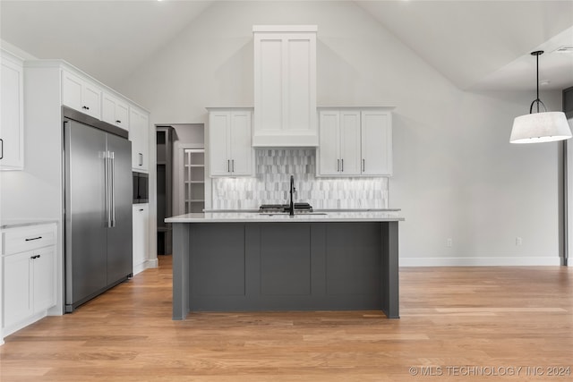 kitchen with stainless steel built in fridge, pendant lighting, light hardwood / wood-style floors, an island with sink, and white cabinets