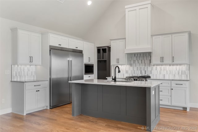 kitchen featuring built in appliances, a center island with sink, sink, high vaulted ceiling, and white cabinets