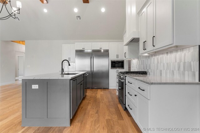 kitchen with white cabinetry, built in appliances, premium range hood, sink, and a center island with sink