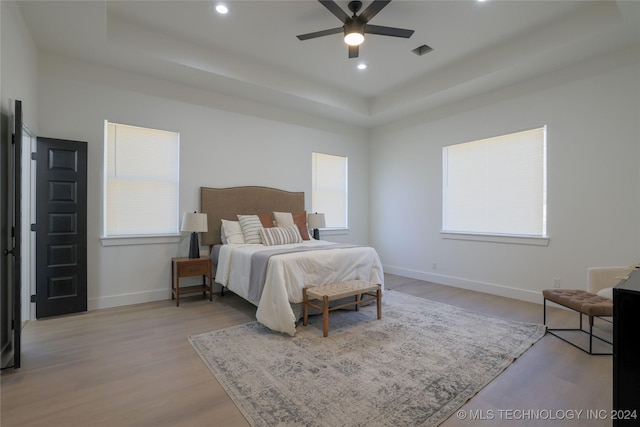 bedroom featuring light hardwood / wood-style flooring, a raised ceiling, and ceiling fan