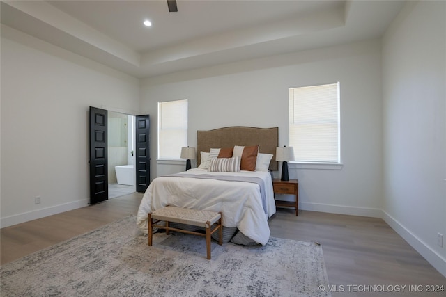 bedroom featuring a raised ceiling, ensuite bathroom, ceiling fan, and light wood-type flooring