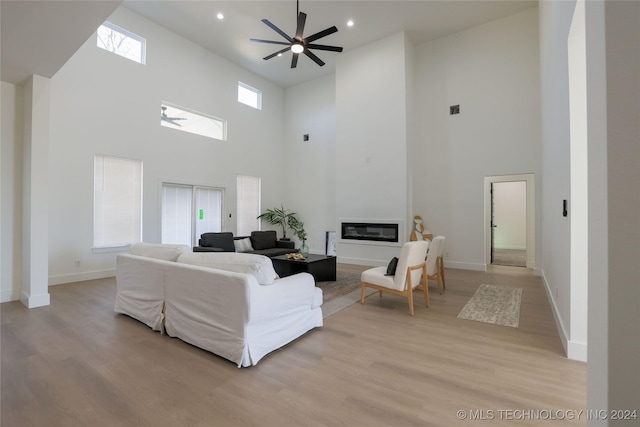 living room featuring a towering ceiling, light hardwood / wood-style floors, and ceiling fan