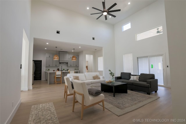 living room with ceiling fan, light hardwood / wood-style floors, and a high ceiling