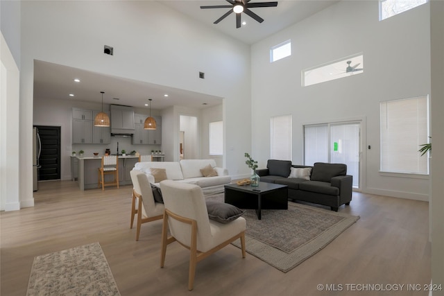 living room featuring ceiling fan, light hardwood / wood-style floors, and a high ceiling