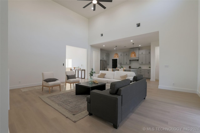 living room with light wood-type flooring, a towering ceiling, and ceiling fan