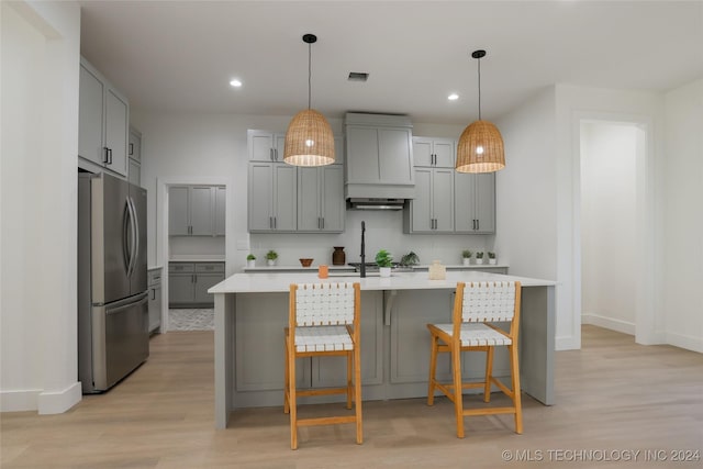 kitchen with gray cabinetry, light hardwood / wood-style flooring, stainless steel fridge, an island with sink, and custom range hood