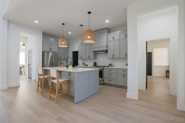 kitchen with light hardwood / wood-style flooring, an island with sink, stainless steel appliances, and custom range hood