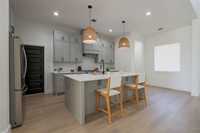 kitchen featuring gray cabinetry, stainless steel fridge, pendant lighting, a kitchen island with sink, and light wood-type flooring