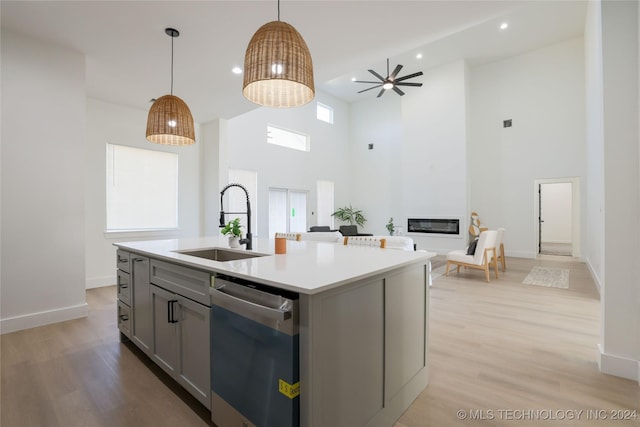 kitchen with light wood-type flooring, stainless steel dishwasher, a kitchen island with sink, sink, and gray cabinets