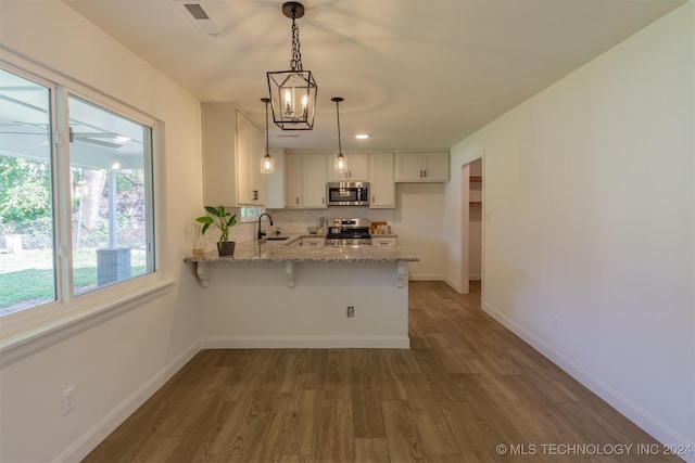 kitchen featuring light stone counters, stainless steel appliances, white cabinetry, kitchen peninsula, and a kitchen breakfast bar