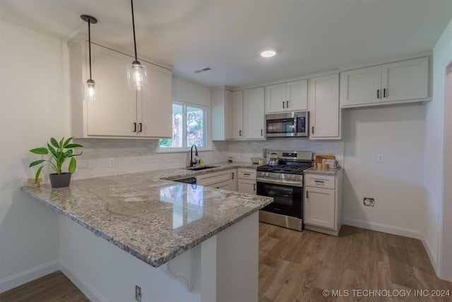 kitchen with light stone counters, kitchen peninsula, stainless steel appliances, and white cabinets