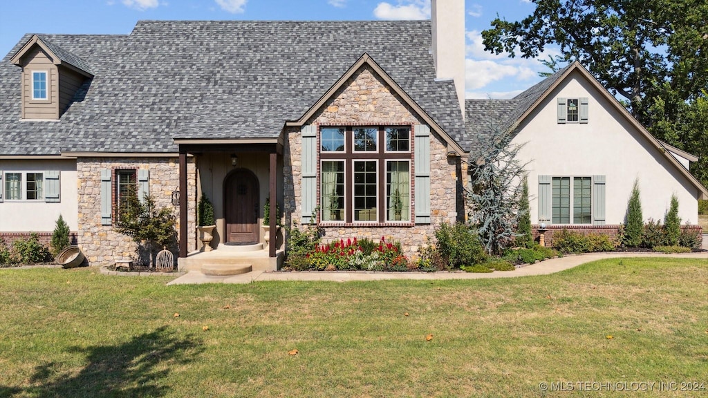 tudor home featuring a front yard, stone siding, roof with shingles, and stucco siding